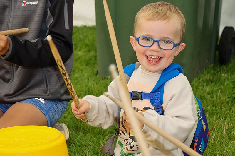 child hitting a bucket with drum sticks